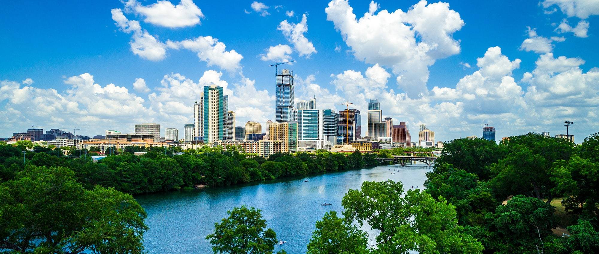 Gorgeous green summer view above tree tops with drone view Travel destination town lake , water , and bridges Austin Texas growing downtown skyline cityscape aerial drone view  tower Modern urban skyscraper rises above the rest Green summer Texas landscape high above Austin Texas growing downtown skyline cityscape aerial drone view from west side of Austin