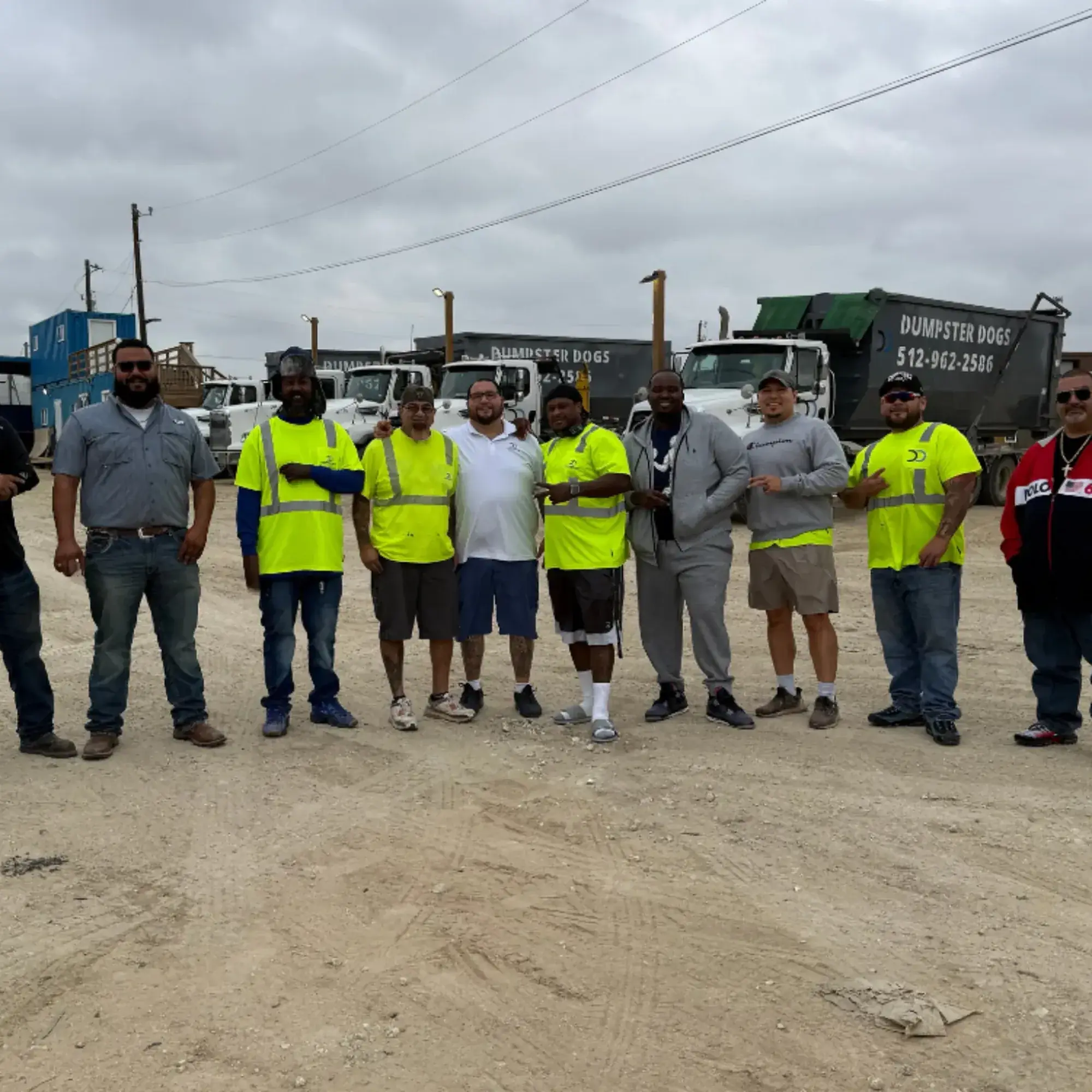 Dumpster Dogs team standing in front of roll-off dumpster trucks at the yard